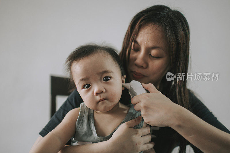 telemedicine asian  chinese mother checking her baby boy son body temperature using thermometer while consulting her pediatrician doctor online using laptop